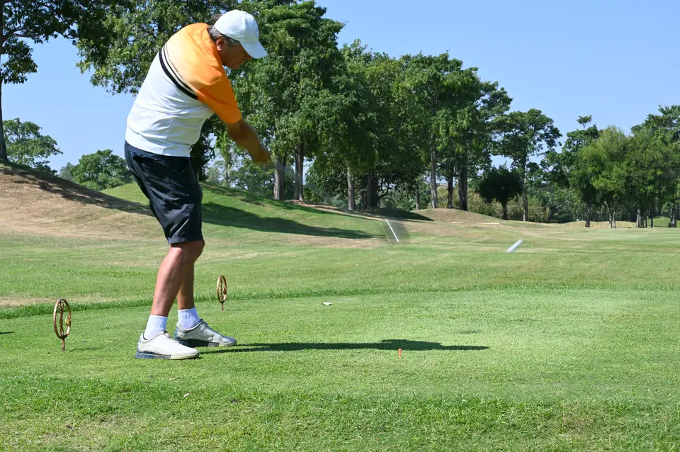A golfer teeing off on a tree-lined fairway